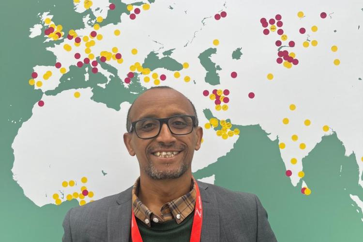 Getaneh Alemu, standing in front of a map showing the UK, Europe, and Africa.