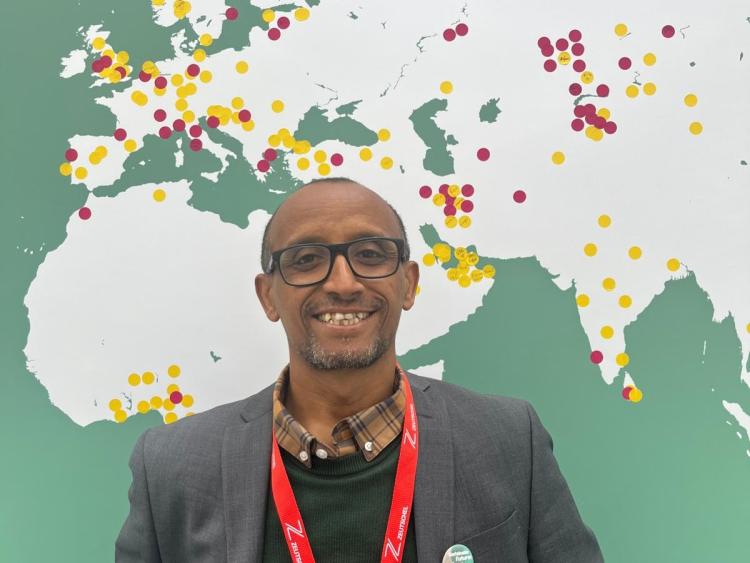 Getaneh Alemu, standing in front of a map showing the UK, Europe, and Africa.