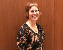Jessica Grzegorski in 2024: smiling and standing against a wood panelled wall 
