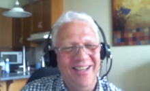 Thomas Brenndorfer, a man with solver hair and rimless glasses, with a broad smile and wearing a headset